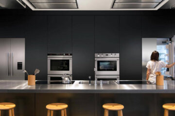 A woman opening a refrigator in a kitchen full of Fisher and Paykel appliances.