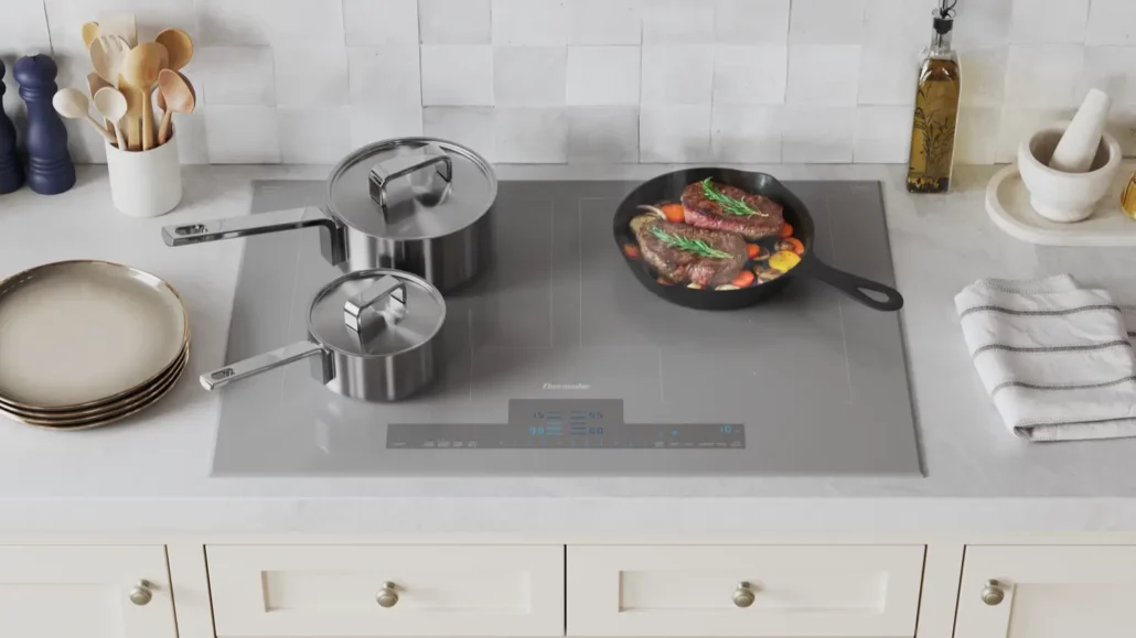 Thermador Liberty CIT367YG 36-inch induction cooktop with HeatShift technology showing three cooking zones with steak in cast iron pan, stainless steel cookware on white countertop