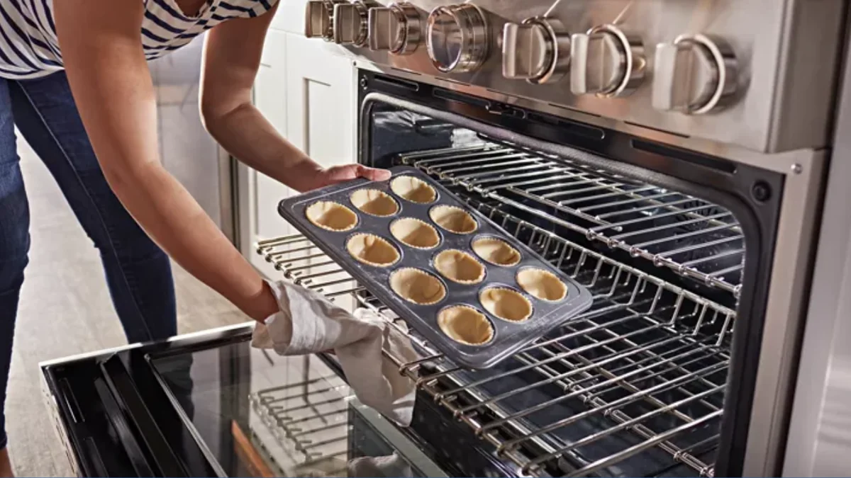 Person using KitchenAid KFDC506JSS oven with SatinGlide rack system, showing muffins baking on multiple racks