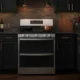 GE Profile double oven gas range installed in modern kitchen with dark cabinetry and brass accents