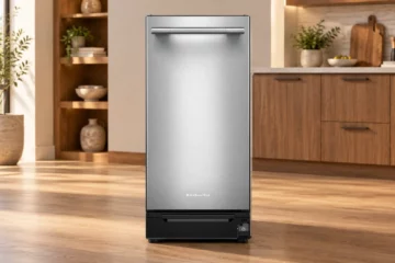 KitchenAid KTTP515TSS stainless trash compactor displayed in an illustrative wood-cabinet kitchen showroom