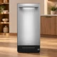 KitchenAid KTTP515TSS stainless trash compactor displayed in an illustrative wood-cabinet kitchen showroom